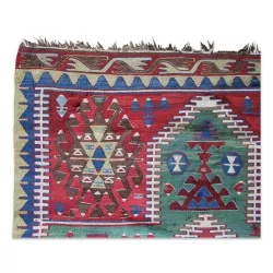 Un tapis "Kilim" en laine, coloris vert, rouge, bleu, noir et blanc.